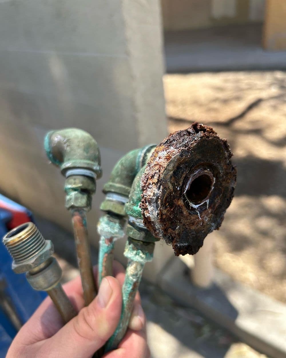 Rusty pipe fittings and connectors held in hand, showing corrosion and wear.