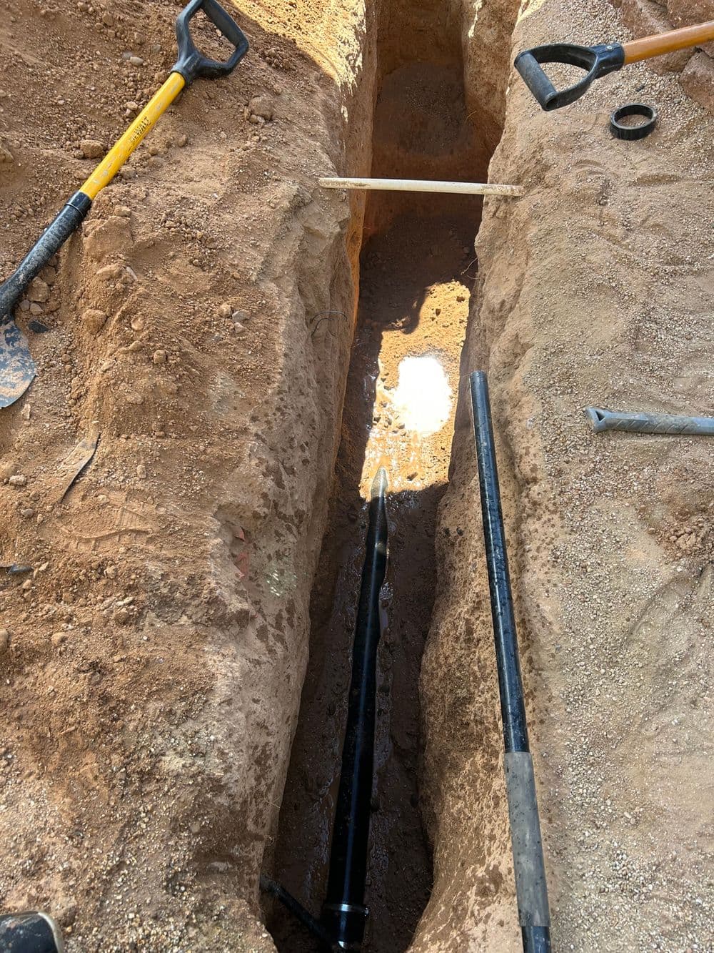 Excavation trench with tools, showing a pipe and earthy surroundings on a construction site.